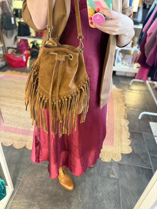 Person holding a brown suede handbag with fringe tasselling in a store setting