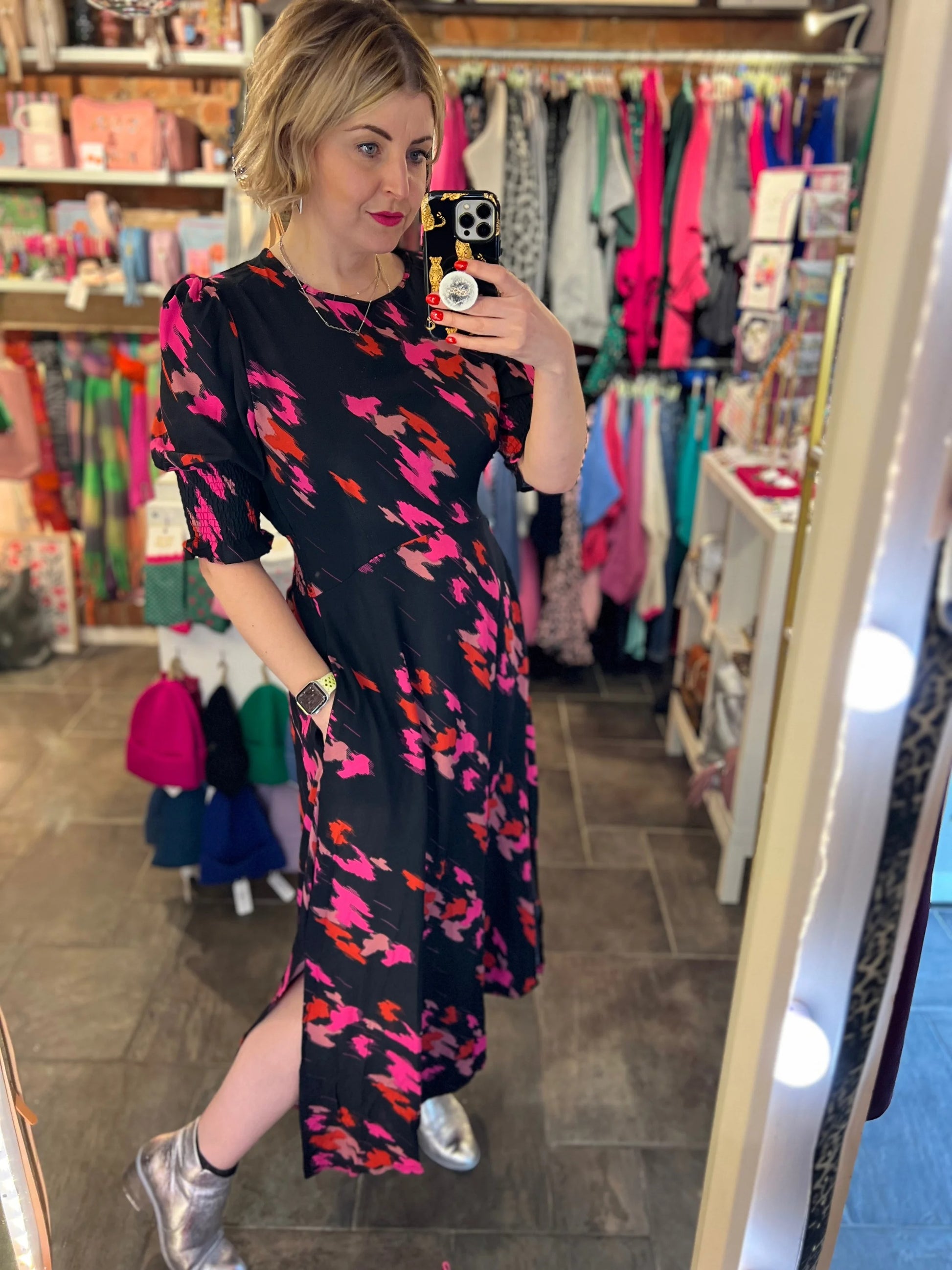 Woman taking a mirror selfie wearing a floral dress in a clothing store.