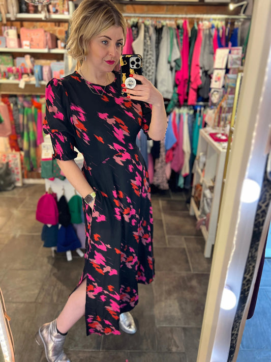 Woman taking a mirror selfie wearing a floral dress in a clothing store.
