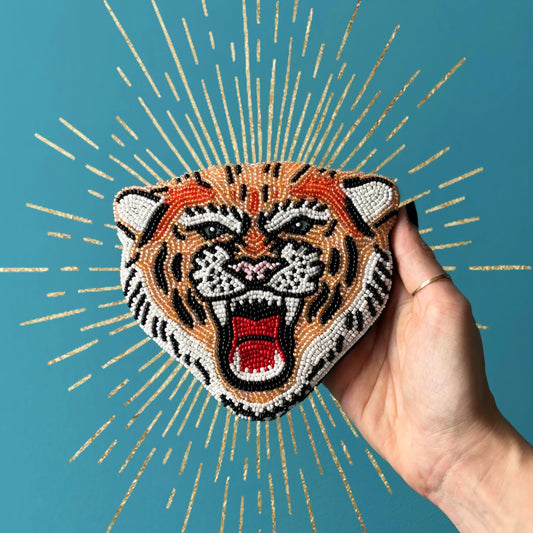 Hand holding a beaded tiger head patch against a blue background with gold accents