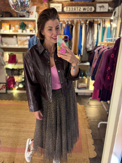 Woman taking a mirror selfie in a clothing store wearing a brown leather jacket, pink top, and leopard print patterned tulle skirt.