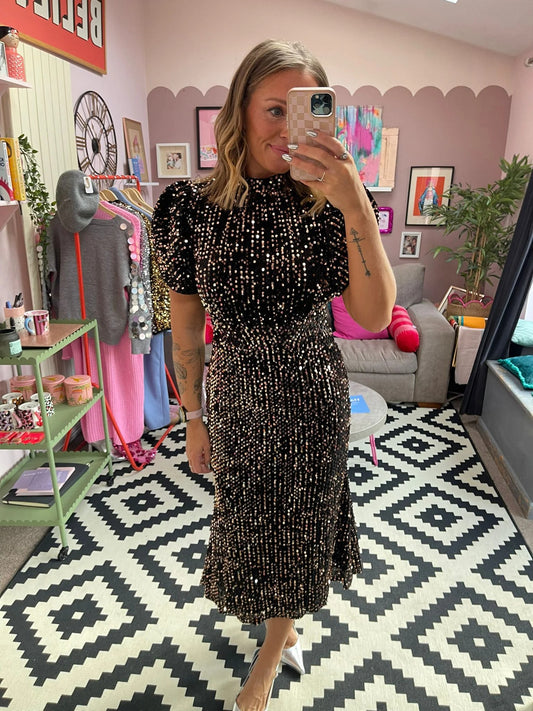 Person taking a mirror selfie wearing a black sequin dress in a room with colorful decor.