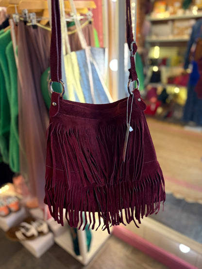 Maroon/ Burgundy suede handbag with fringe details in a store setting