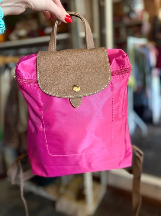 Pink bag with a brown flap held by a hand against a blurred indoor background