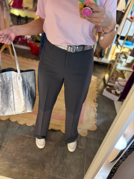 Person wearing a pink shirt and dark grey tailored trousers holding a silver handbag in a store setting.