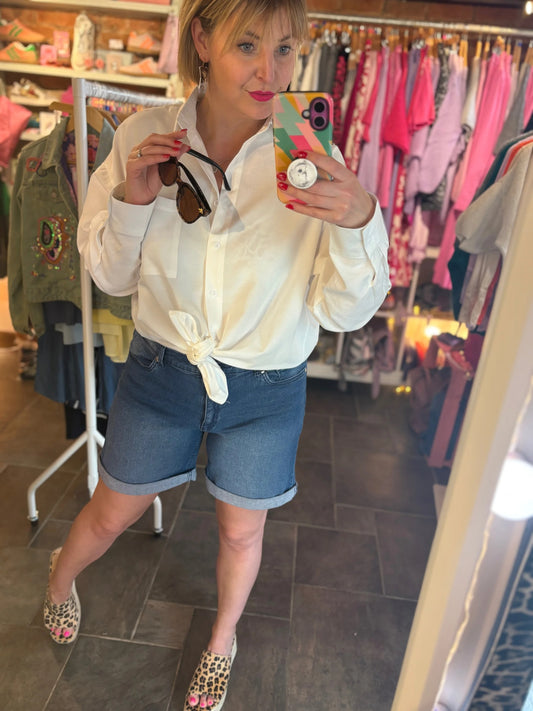 Person taking a mirror selfie wearing a white shirt and denim shorts in a clothing store.