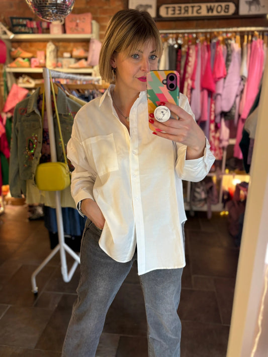 Person taking a mirror selfie in a clothing store wearing a white shirt and gray pants.