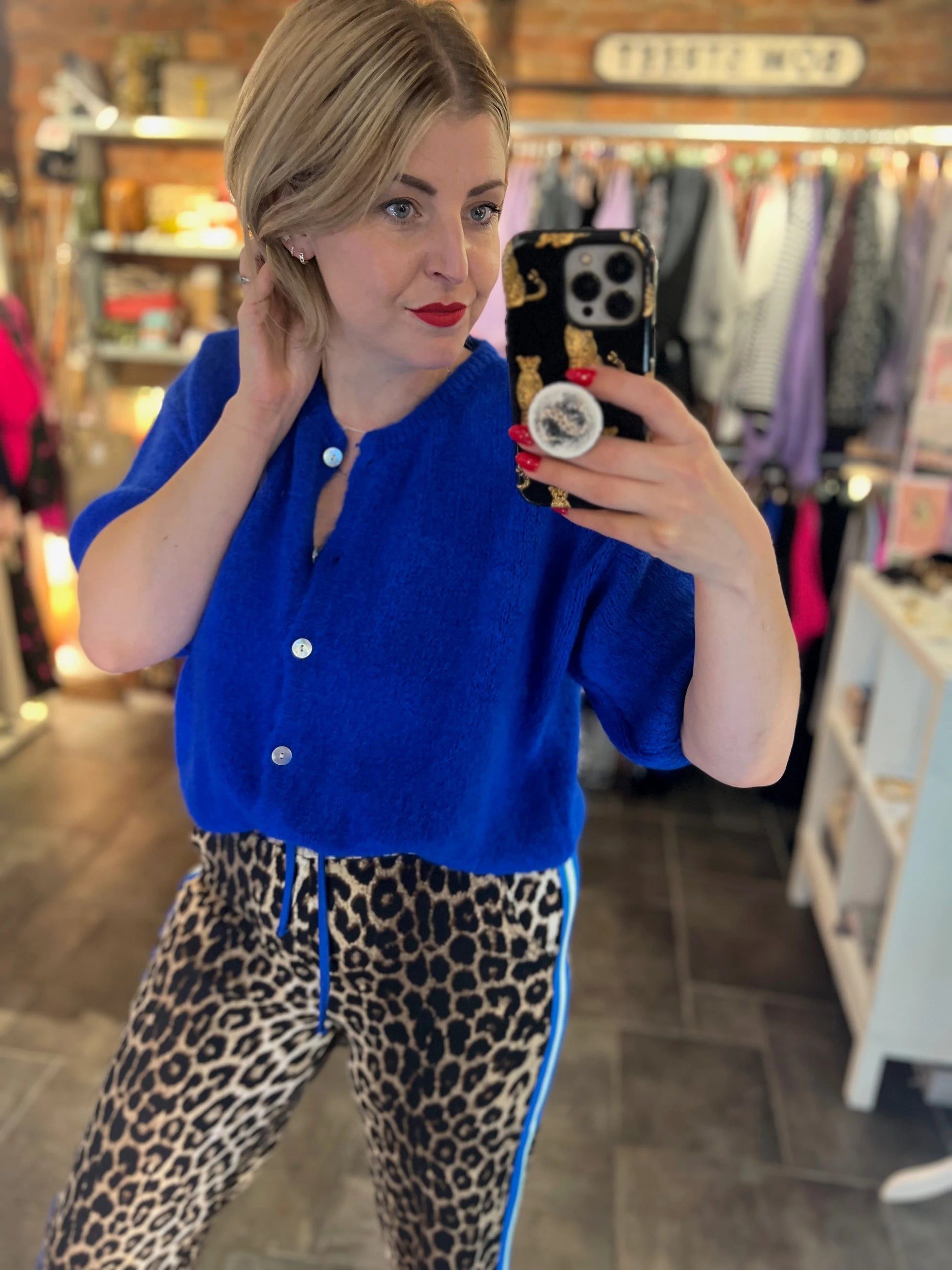 Woman taking a mirror selfie wearing a blue top and leopard print pants in a store.