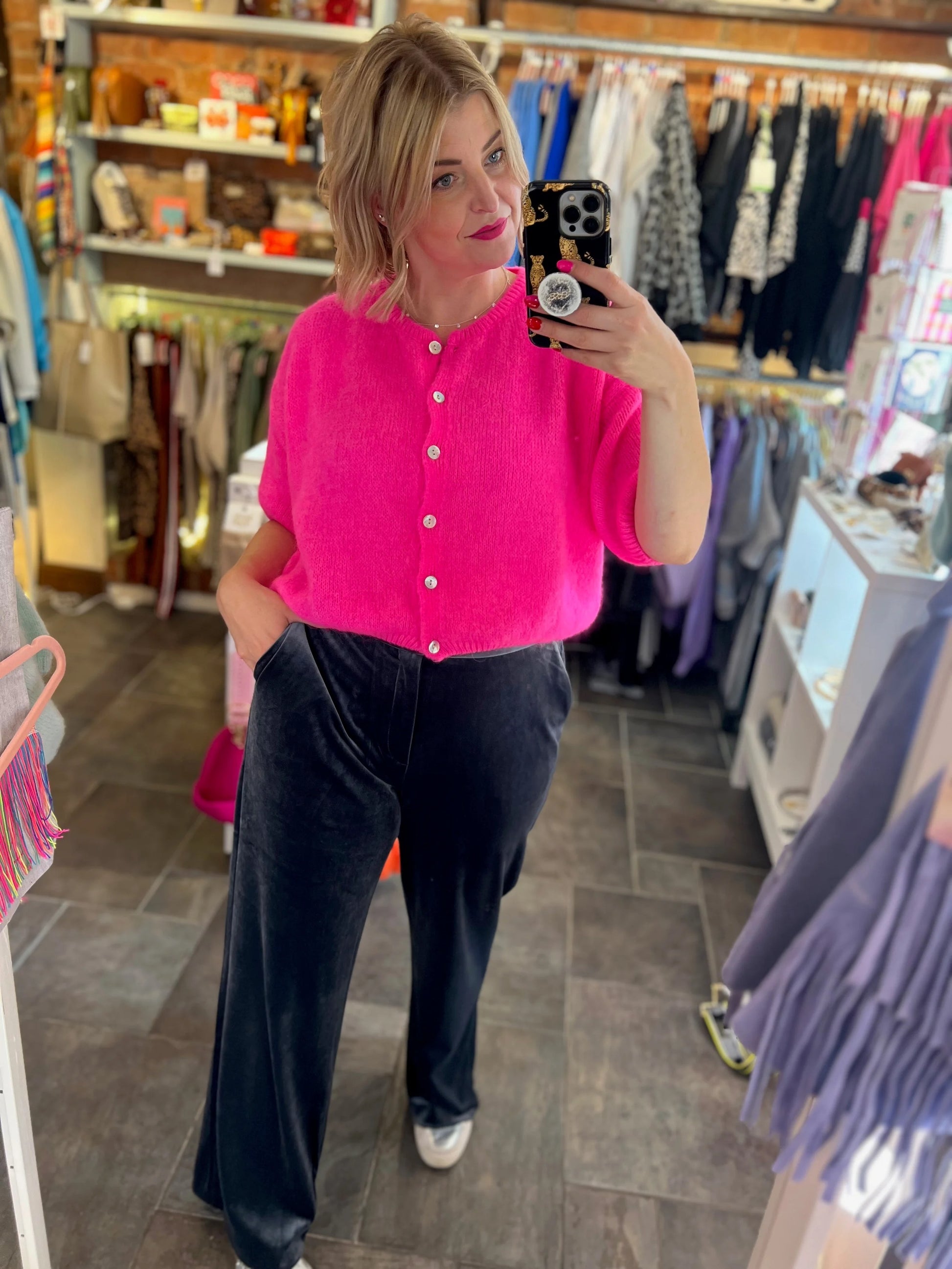 Person taking a mirror selfie wearing a bright pink shirt and black pants in a store.
