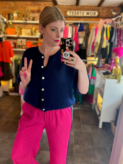 Woman taking a mirror selfie in a clothing store wearing a navy cardigan and pink pants.