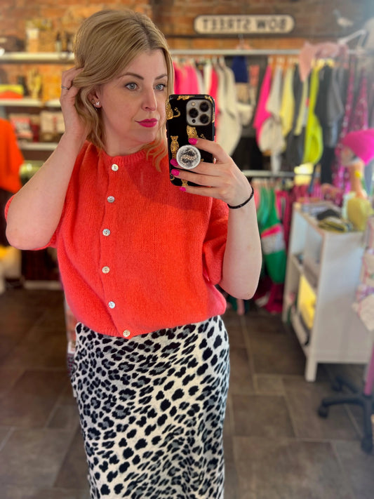 Woman taking a mirror selfie wearing an orange cardigan and leopard print skirt in a store.
