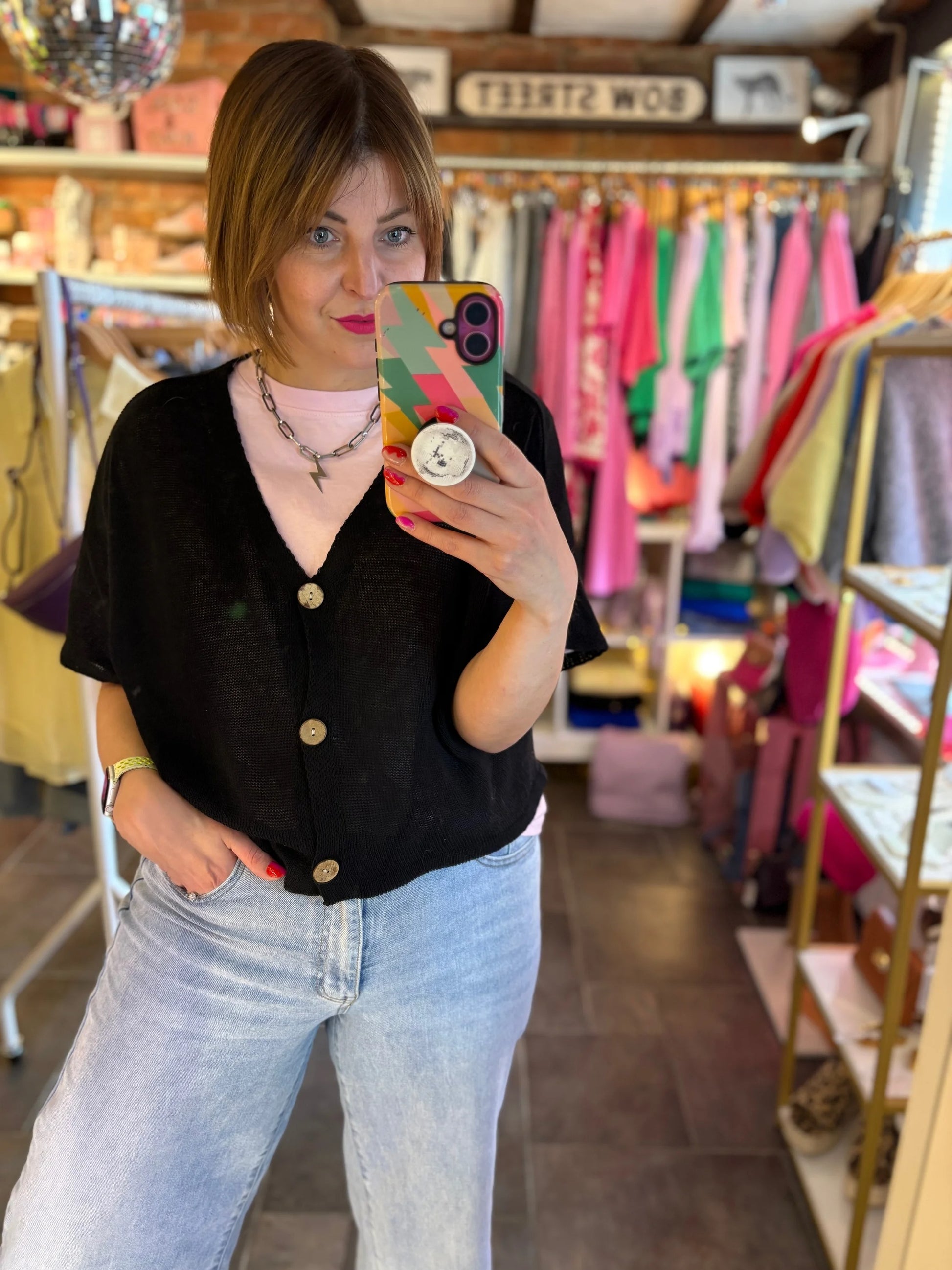 Person taking a mirror selfie in a clothing store wearing a black top and light blue jeans.