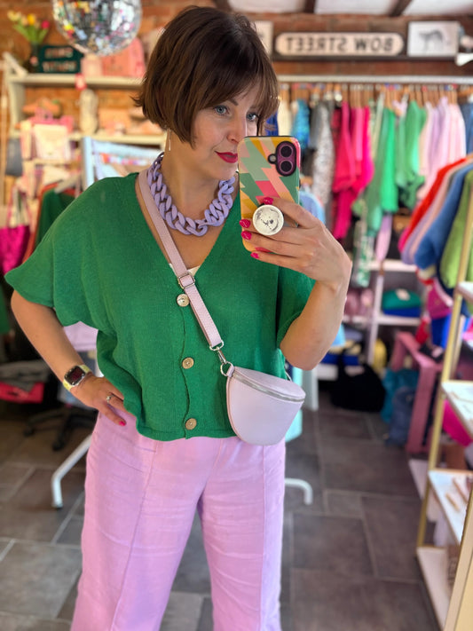 Person taking a mirror selfie wearing a green top and pink pants in a store.