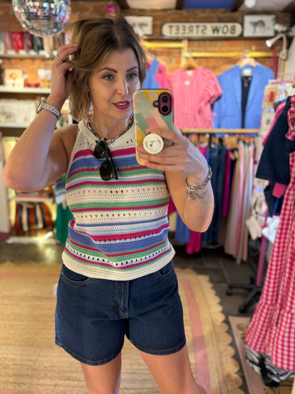 Woman taking a mirror selfie wearing a colorful striped sleeveless top and denim shorts in a clothing store.