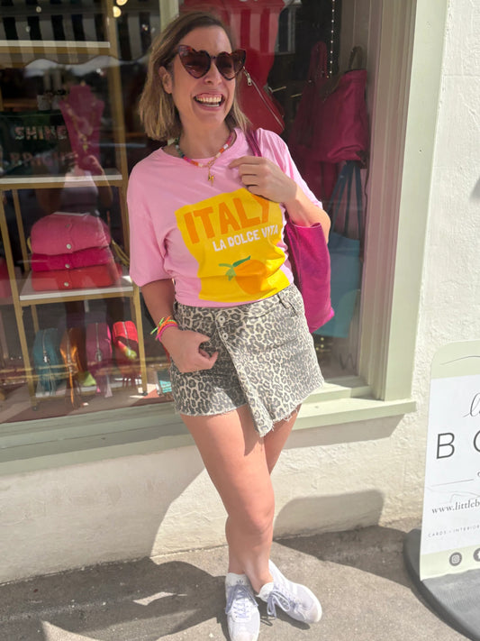 Woman wearing a pink t-shirt with a yellow graphic and leopard print shorts standing in front of a store window.