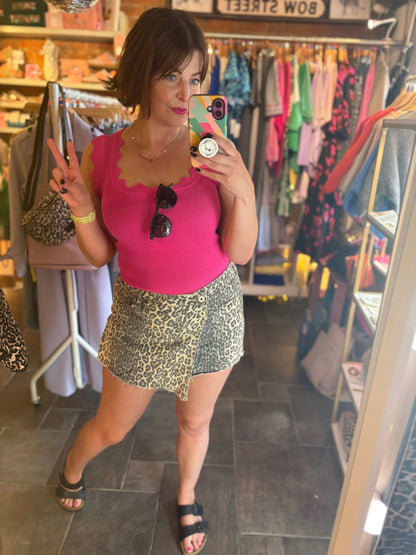 Woman taking a mirror selfie in a clothing store wearing a pink top and patterned skirt.