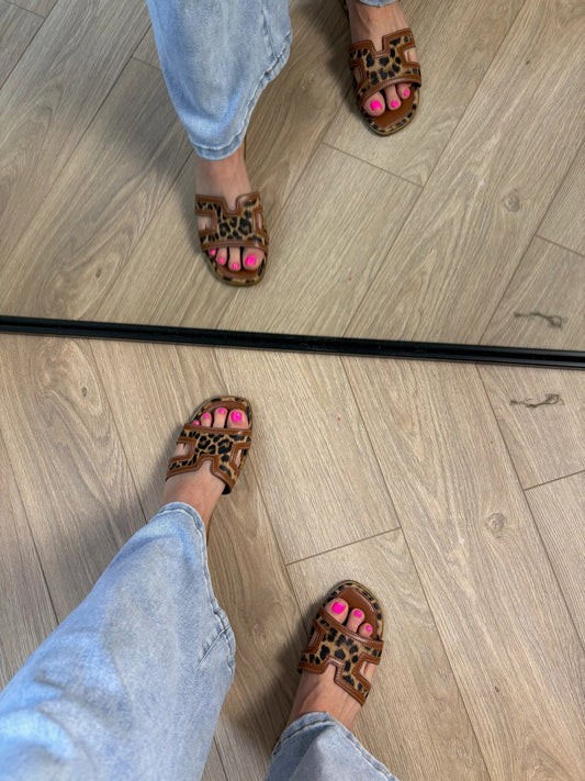 Person wearing leopard print sandals with pink accents on a wooden floor.