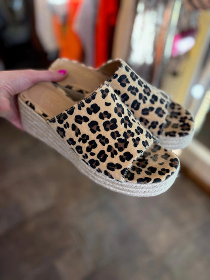 Leopard print wedge sandals held by a hand with pink nail polish.
