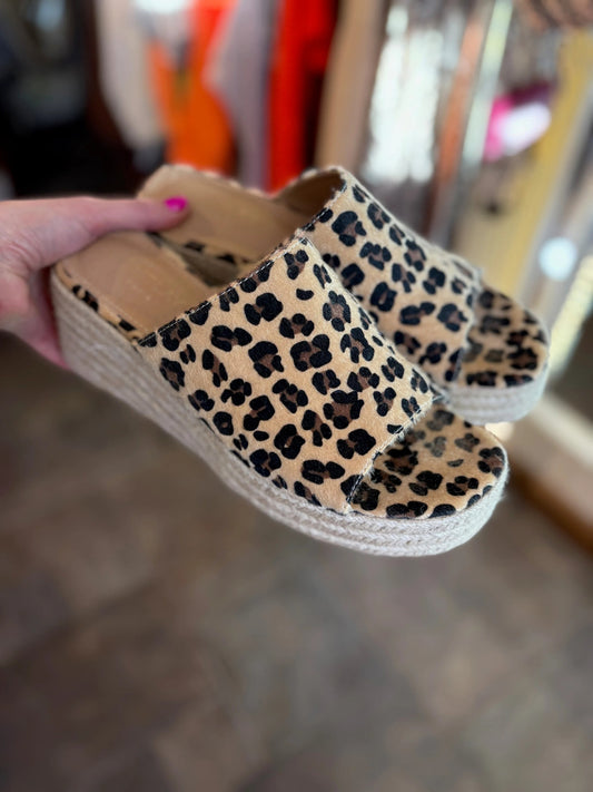 Leopard print wedge sandals held by a hand with pink nail polish.