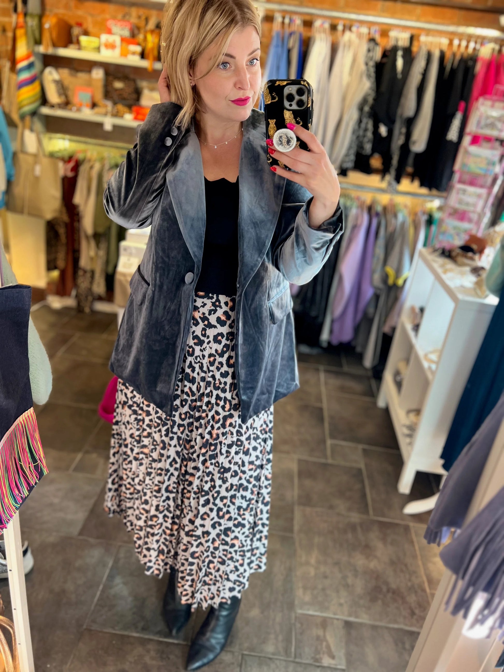 Woman taking a mirror selfie in a clothing store wearing a denim jacket and leopard print dress.