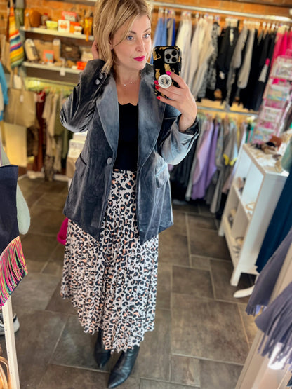 Woman taking a mirror selfie in a clothing store wearing a denim jacket and leopard print dress.