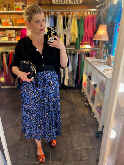 Woman taking a mirror selfie in a clothing store wearing a black top and blue leopard print skirt.
