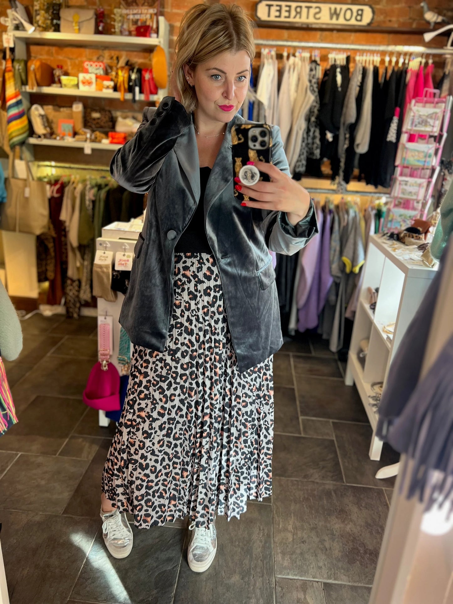 Woman taking a mirror selfie in a clothing store wearing a gray blazer and leopard print skirt.
