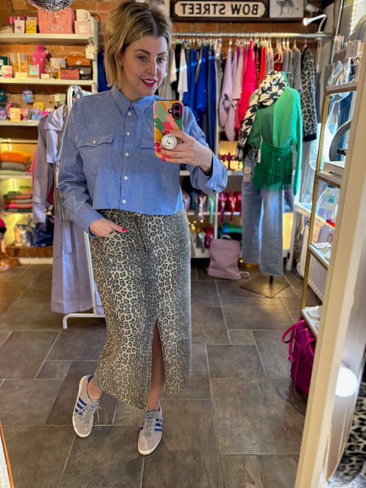 Woman taking a mirror selfie in a clothing store wearing a blue shirt and patterned skirt.