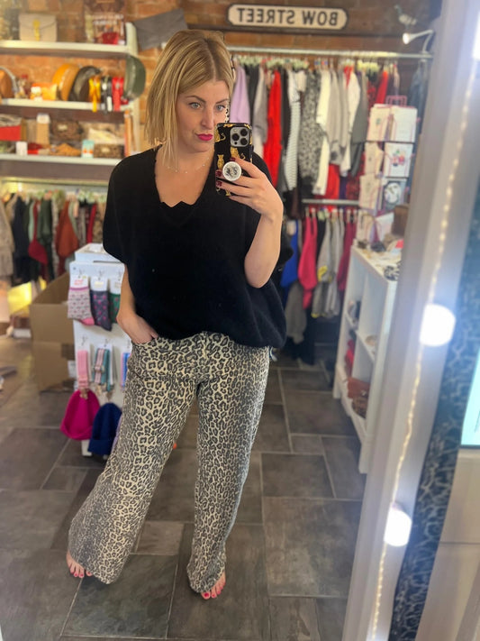 Woman taking a mirror selfie wearing a black top and leopard print pants in a store.