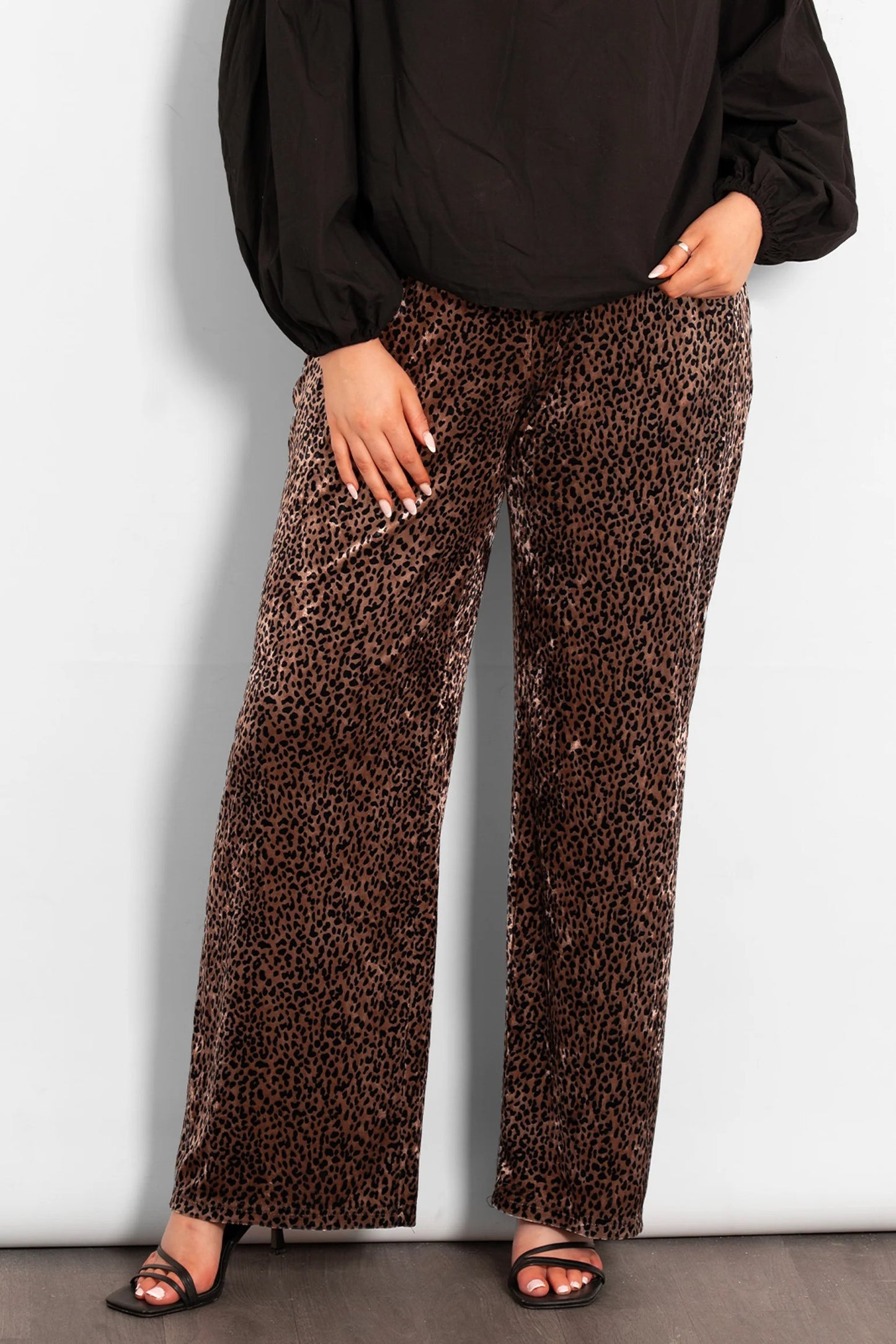 Person wearing a black top and leopard print pants against a white wall.