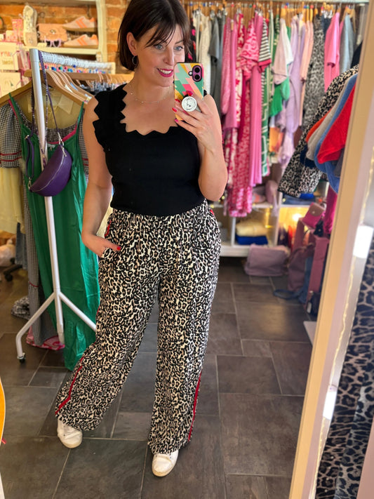 Woman taking a mirror selfie wearing a black top and leopard print pants in a clothing store.