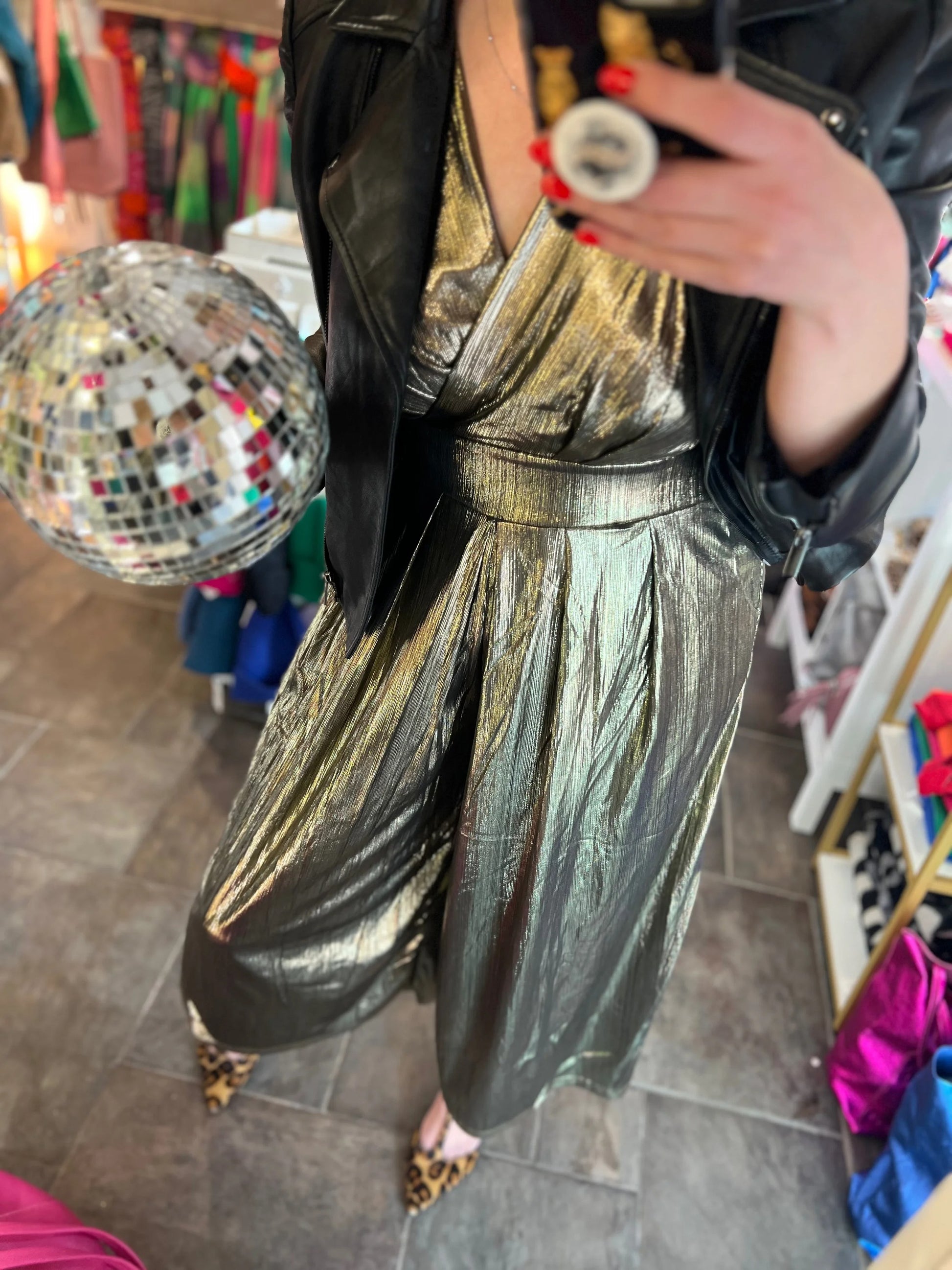 Person wearing a gold metallic jumpsuit holding a disco ball in a store setting.