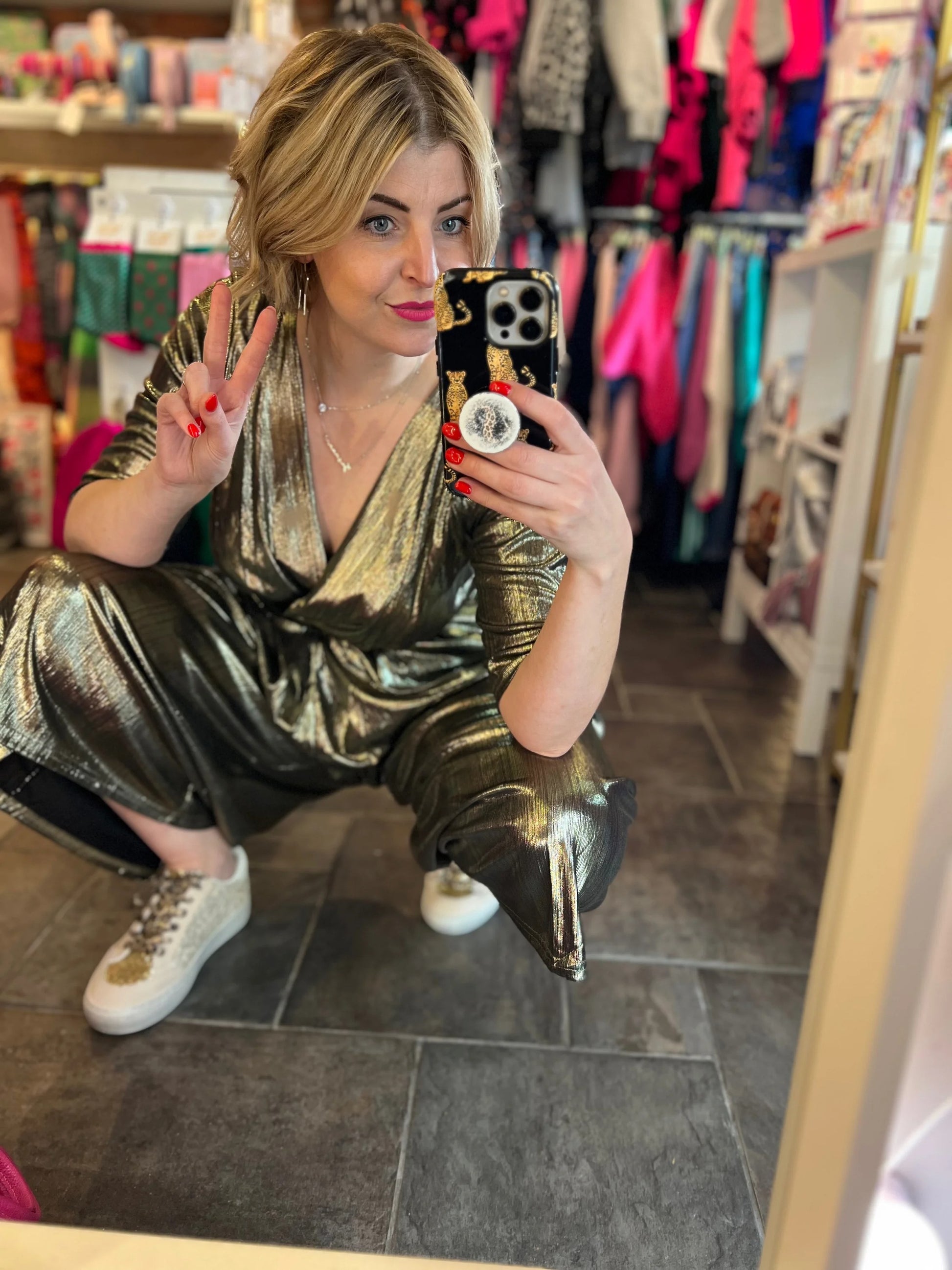 Woman in a gold sequin outfit taking a mirror selfie in a store.