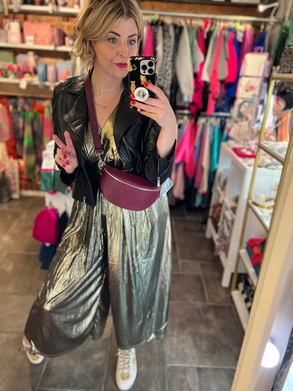 Person taking a mirror selfie in a store wearing a black leather jacket and metallic pants.