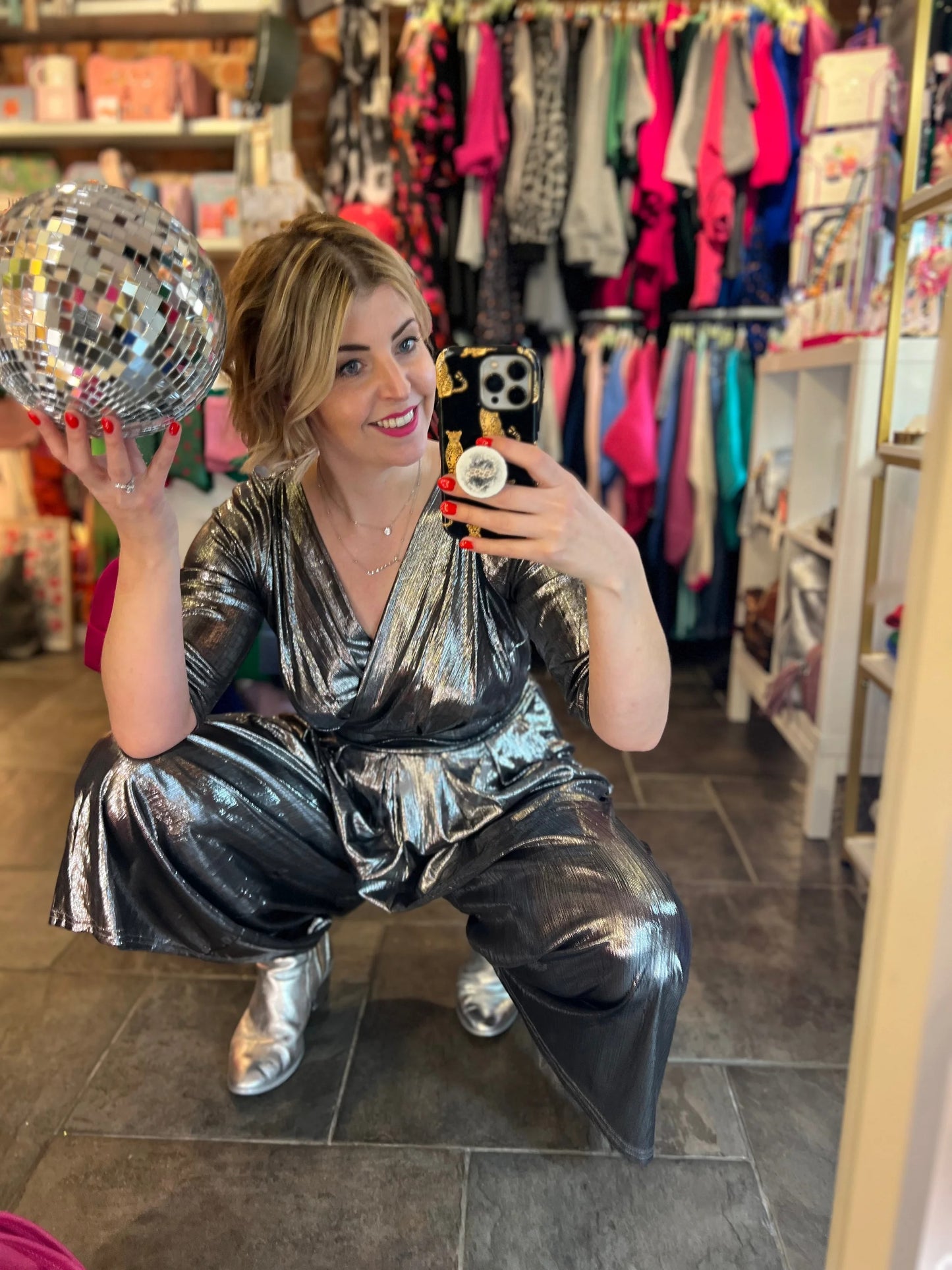Woman in a silver jumpsuit holding a disco ball in a store.