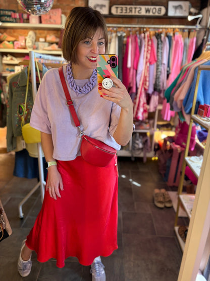 Person taking a mirror selfie in a clothing store wearing a red skirt and pink top.