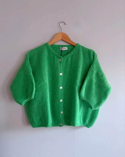 Green cardigan on a wooden hanger against a white background