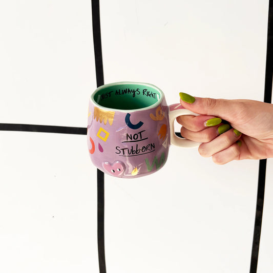 Person holding a colorful mug with text against a white background