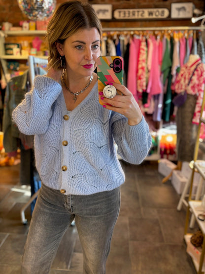Woman taking a mirror selfie wearing a light blue cardigan and gray pants in a store.