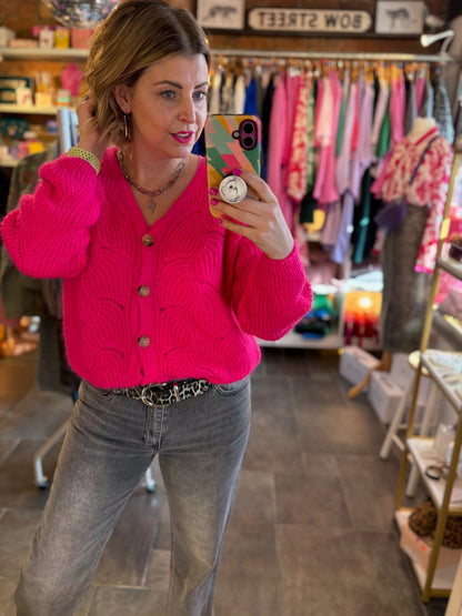 Woman taking a mirror selfie wearing a bright pink cardigan in a store.