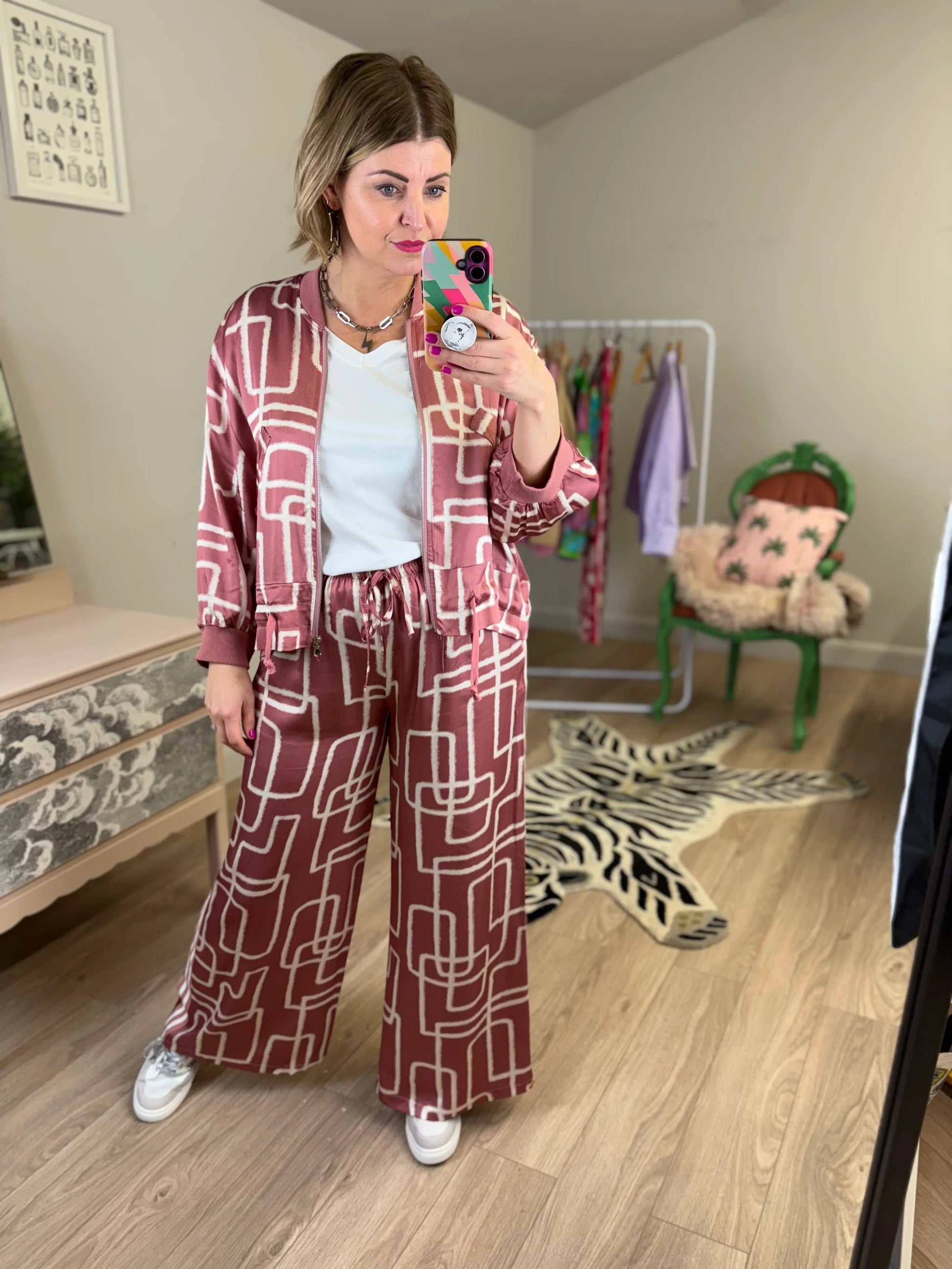 Woman taking a mirror selfie wearing a patterned outfit in a room with a child's chair and toys.