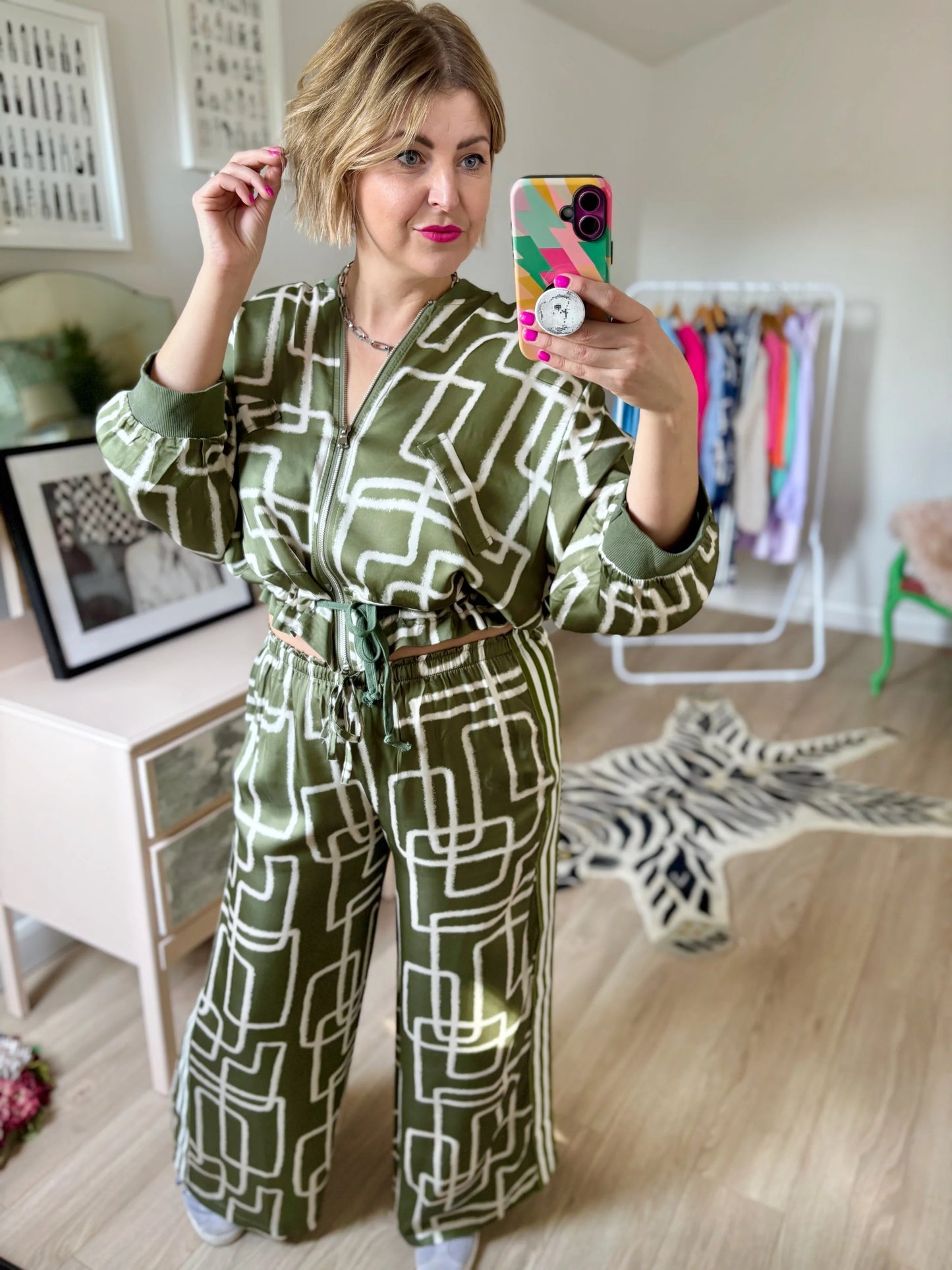 Woman taking a mirror selfie wearing a green patterned jumpsuit in a room with a zebra rug.