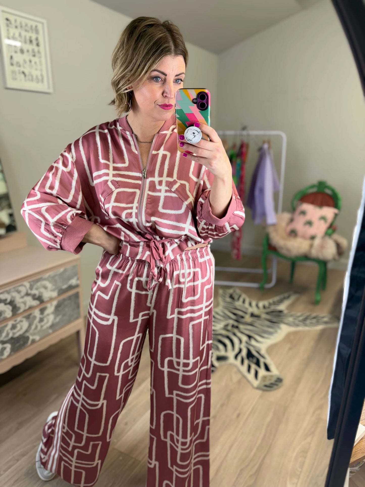 Woman taking a mirror selfie wearing a pink and white geometric patterned outfit in a room.