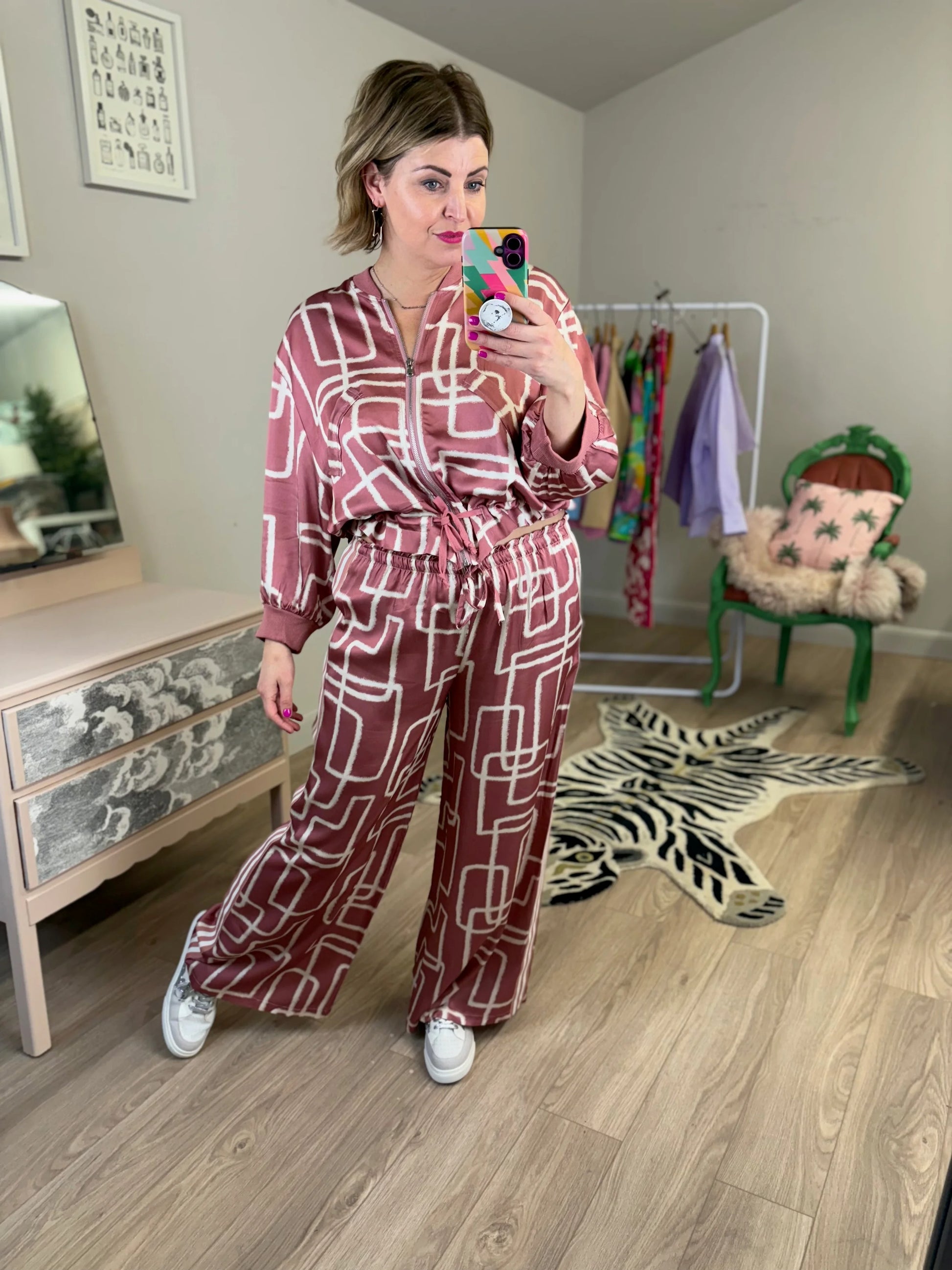 Woman taking a mirror selfie wearing a patterned outfit in a room with furniture and decor.