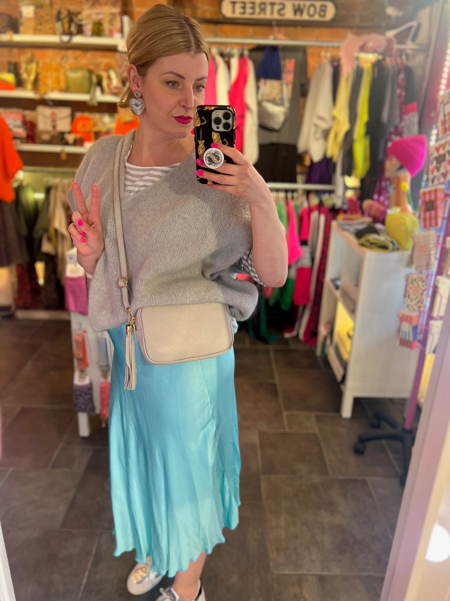 Woman taking a mirror selfie in a clothing store wearing a gray sweater and light blue skirt.