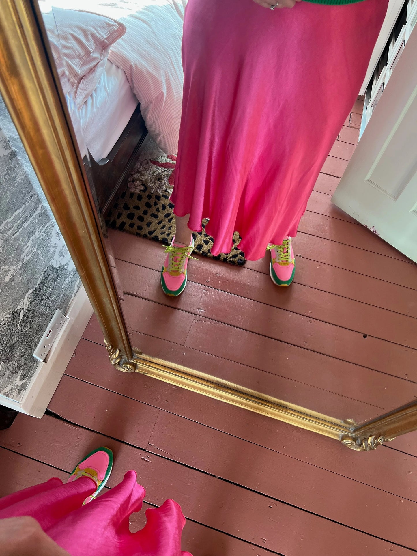 Person wearing a bright pink dress and colorful shoes standing in front of a mirror on a wooden floor.