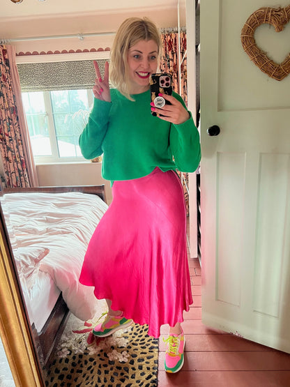 Person wearing a green sweater and pink skirt in a room with a bed and window.