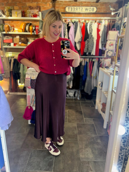 Woman taking a mirror selfie in a clothing store wearing a red sweater and dark skirt.