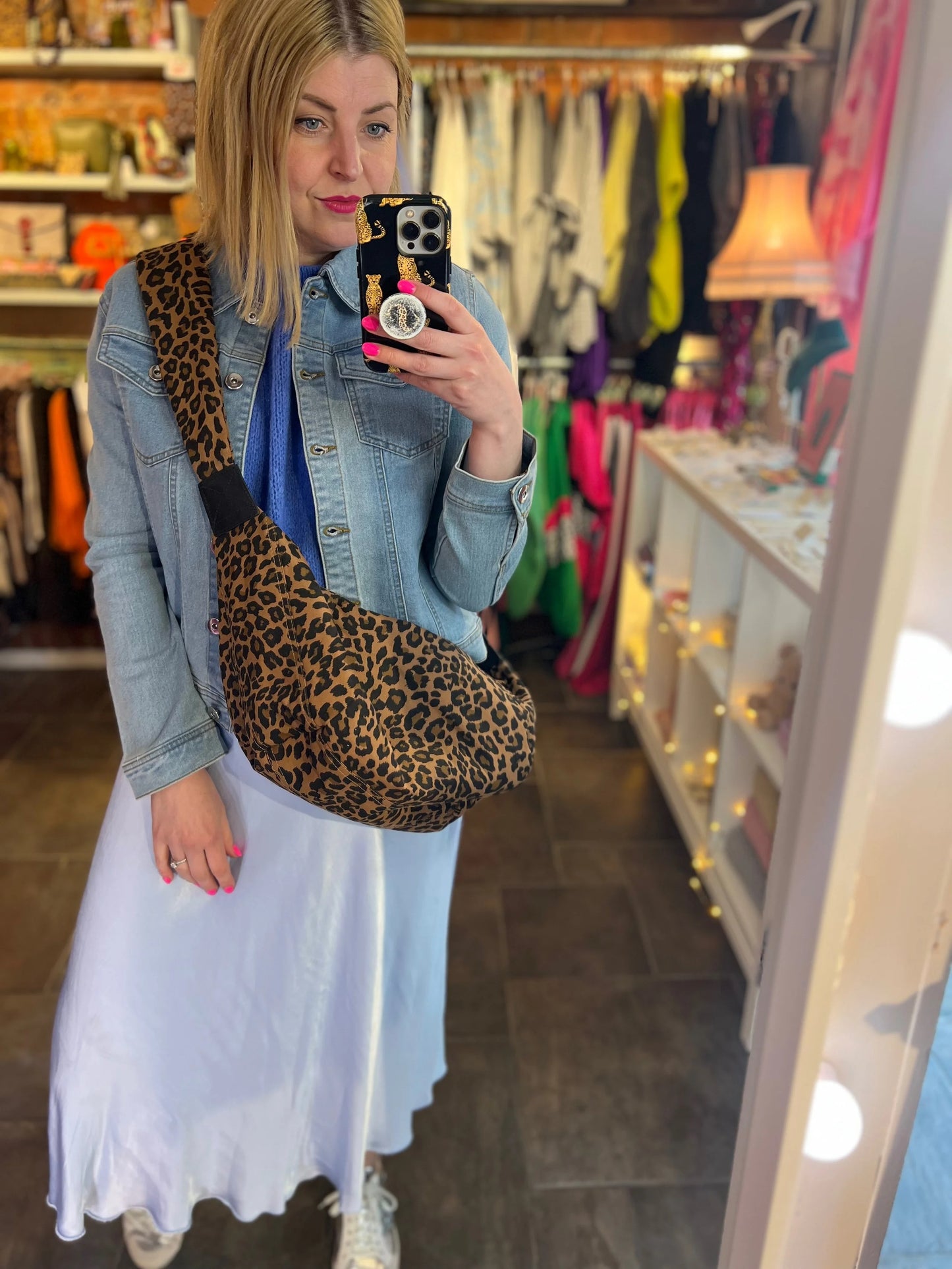 Person taking a mirror selfie wearing a leopard print bag in a store.
