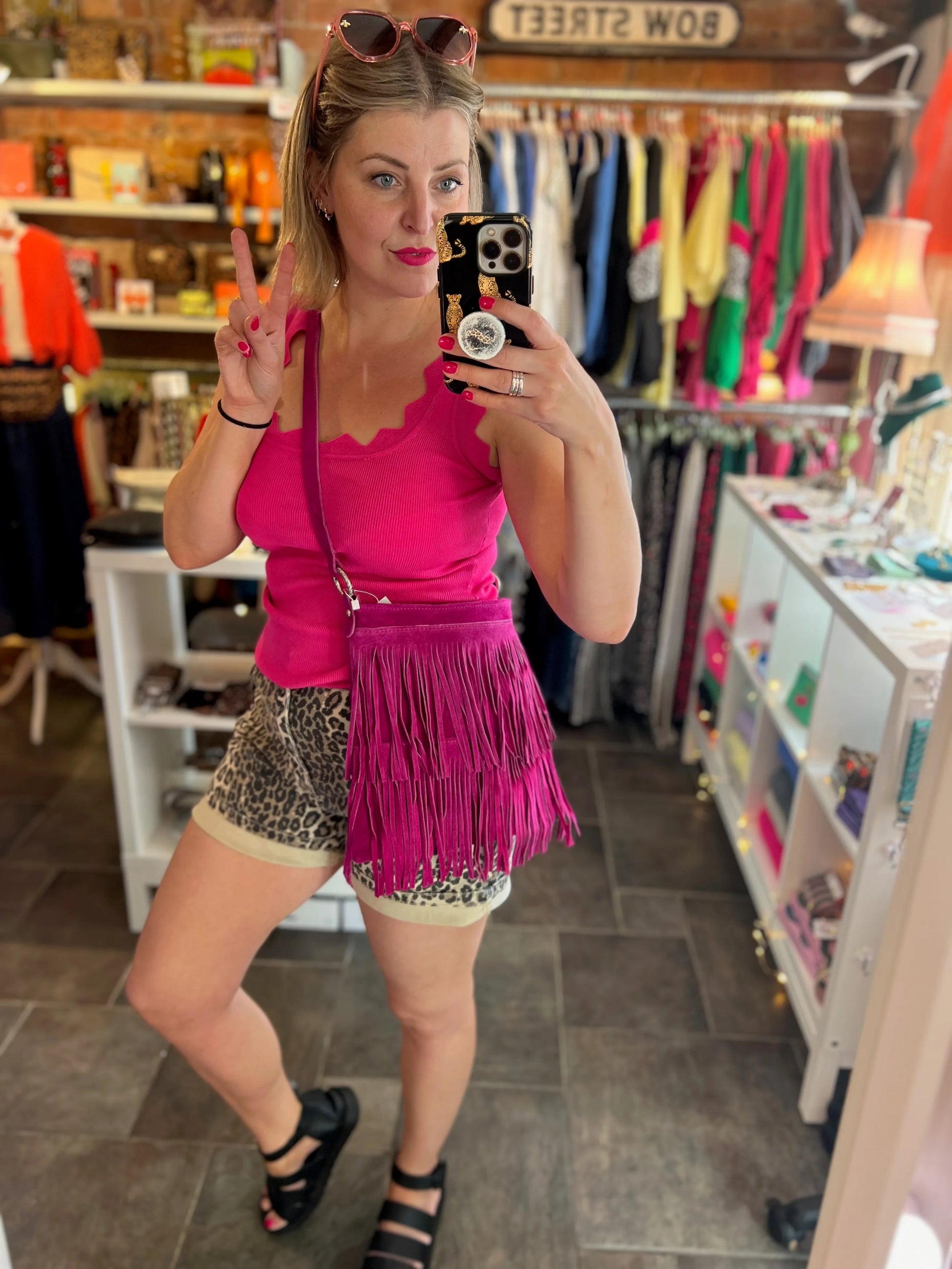Woman taking a mirror selfie wearing a pink top and fringed skirt in a store.